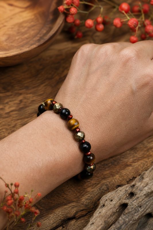 A close‑up of a hand wearing a handcrafted crystal bracelet with black tourmaline, tiger eye, and pyrite beads on a natu