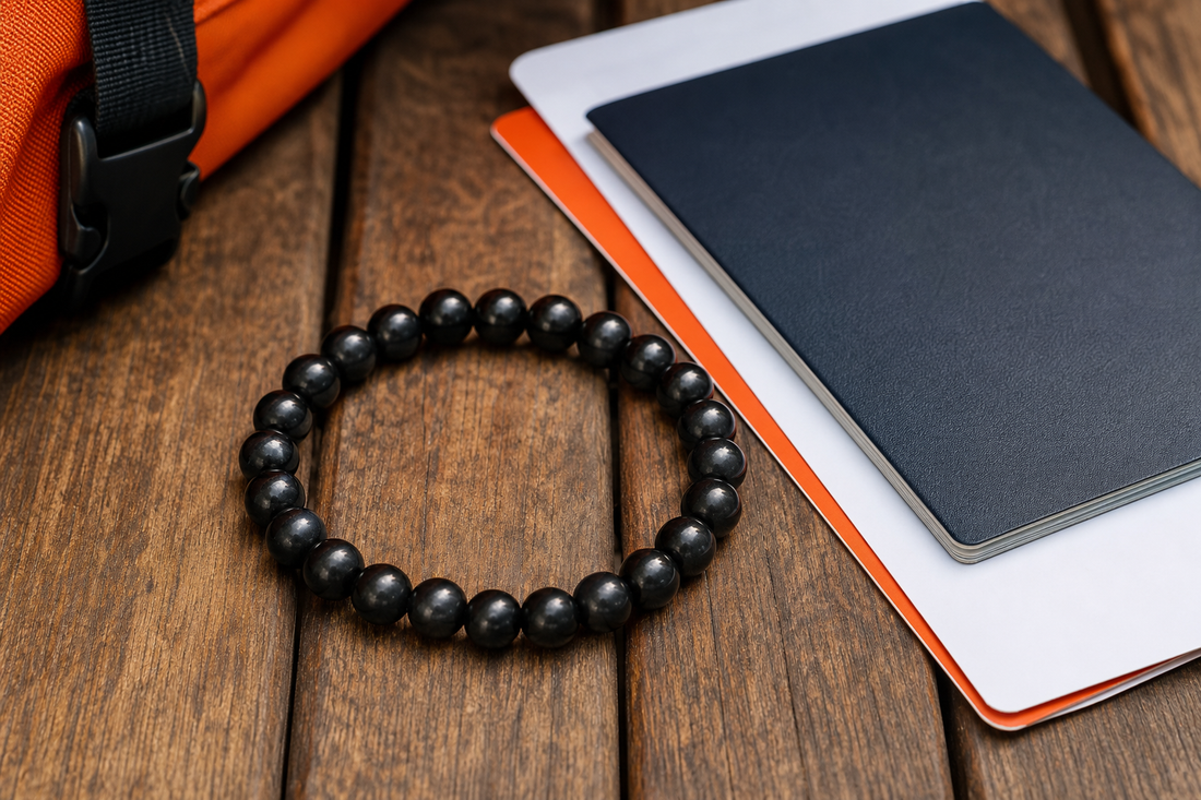 A realistic close‑up of a black shungite bracelet on a wooden travel table, with a passport and boarding pass beside it,